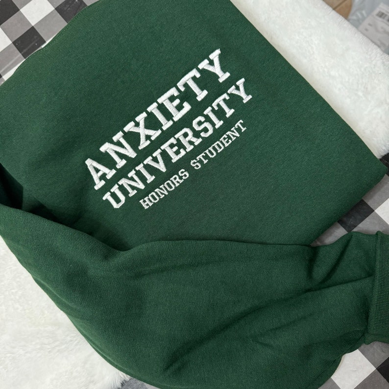 May include: A dark green sweatshirt with the text "ANXIETY UNIVERSITY HONORS STUDENT" embroidered in white.