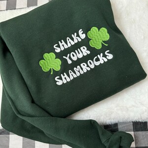 May include: Green sweatshirt with white embroidered text that says "Shake Your Shamrocks" and two green shamrock designs.