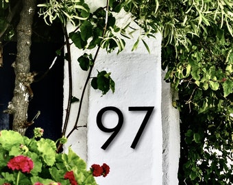 May include: A white wall with the number 97 painted in black. The wall is covered in green foliage.