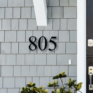 May include: Black house number plaque with the number 805 on a gray siding background.