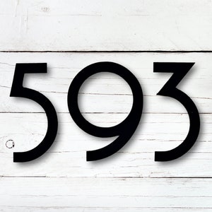 May include: Black metal house numbers, displaying the digits 593, are set against a white wooden plank background. The numbers have a modern, sans-serif font and cast a subtle shadow, enhancing their three-dimensional appearance.
