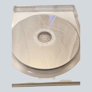 May include: A stack of silver PS3 game discs inside a clear plastic case. The discs have a reflective surface and the PS3 logo is visible. The case is open, revealing the discs.