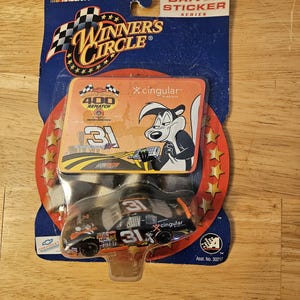May include: A black and orange NASCAR die-cast car with the number 31 on the side. The car is in a plastic package with a Cingular Wireless logo and a cartoon skunk. The package also says "Winner's Circle" and "Driver Sticker Series".