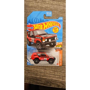 May include: A red and black Hot Wheels toy truck with the number 81 on the side. The packaging includes the Hot Wheels logo, the text "NEW 2021", and the words "HW Hot Trucks".