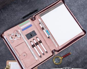 May include: A dusty pink leather portfolio organizer featuring a zippered closure, multiple card slots, a cable organizer strap, a snap-button pocket, three white pens, and a lined notepad. The interior includes a document sleeve and pen loops.