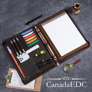 May include: A brown leather zippered binder with a notepad, pens, and other office supplies. The binder has a metal ring system and a zipper closure. The text "Canada EDC" is visible at the bottom of the image.