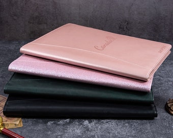 May include: A stack of four leather-like document holders in various colors. The top one is a light pink with the word "Canada" embossed on it, followed by a glittery pink, a dark green, and a black one. The initials "MPH" are embossed on the top right corner of the pink document holder.