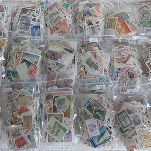 Op de afbeelding: Een verzameling vintage postzegels van over de hele wereld, georganiseerd in doorzichtige plastic zakken. De postzegels zijn in verschillende kleuren en ontwerpen, en sommige hebben handgeschreven labels.