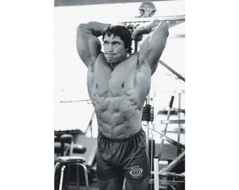 May include: Black and white poster of a bodybuilder flexing his muscles. The bodybuilder wears dark shorts with a logo. Gym equipment is visible in the background. The poster is held by clips at the top.
