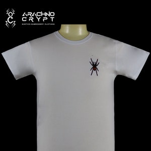 May include: White t-shirt with a black and red spider embroidered on the front. The shirt has the text "Arachno Crypt" and "Exotics Embroidery Clothing" printed on the top left corner.