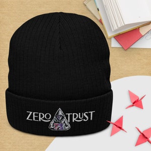 May include: Black knit beanie with a white embroidered logo that says "ZERO TRUST" and a graphic of a hooded figure with a shield.