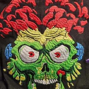 May include: Embroidered green, red and yellow alien skull with a wide open mouth and large eyes. The alien's hair is red and yellow.