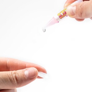 May include: A pink and yellow glue stick with the word "Sticky" printed on it. A drop of glue is being dispensed from the tip of the glue stick.
