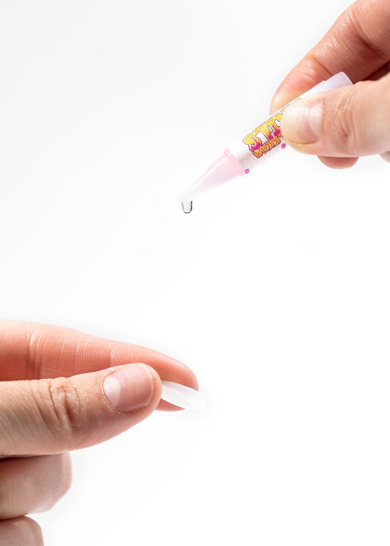 May include: A pink and yellow glue stick with the word "Sticky" printed on it. A drop of glue is being dispensed from the tip of the glue stick.