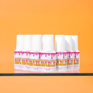 May include: A collection of white nail glue bottles with pink accents and text that reads "Blissful Kream Nail Nails". The bottles are arranged on a glass shelf against an orange background.