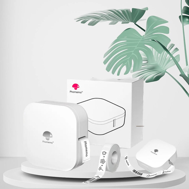 May include: White label maker with a mushroom logo, "Phomemo" printed on the side. It comes with a roll of white label tape with black text and a small, white label dispenser.