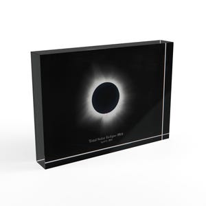 May include: Black acrylic block featuring a total solar eclipse image. The image shows a dark circle surrounded by a bright corona against a black background. The text "Total Solar Eclipse 2024" is visible.