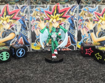 Puede incluir: Una figura en miniatura verde y blanca con alas se encuentra sobre una base negra. La figura está frente a tres cajas con ilustraciones de estilo anime. Dados con símbolos están frente a las cajas.