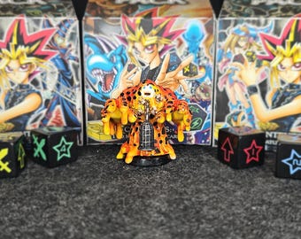 Könnte beinhalten: Eine detaillierte Abbildung einer Sammlerfigur mit einzigartigem Design, in Orange, Gelb und Schwarz. Die Figur ist von schwarzen Würfeln mit verschiedenen Symbolen und Kartenspielboxen im Hintergrund umgeben. Das Thema bezieht sich auf Kartenspiele.