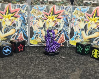 May include: A painted miniature figure of a skeletal creature in a purple robe standing before three boxes featuring anime character artwork. Four black dice with colored symbols including a blue lightning bolt, red star, green star, and yellow wheel.