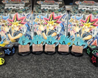 Könnte beinhalten: Eine Sammlung von Yu-Gi-Oh!-Sammelkartensets und Würfeln. Das Wort "FINAL" wird mit blauen und bronzefarbenen Dekorationselementen geschrieben. Die Sets zeigen eine Figur mit stacheligen Haaren und die Würfel haben Sterne und andere Symbole.