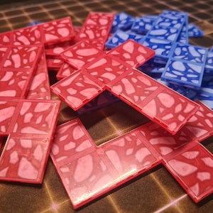 May include: A set of red and blue plastic tiles with a marbled pattern. The tiles are shaped like L's and T's and are designed for a game or puzzle.
