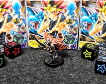 Puede incluir: Figura en miniatura de un guerrero con capa roja y espada, frente a paquetes de cartas de Yu-Gi-Oh!. Dados negros con símbolos coloridos dispersos alrededor de la figura, sugiriendo un tema de juego de mesa.