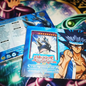 May include: A blue and white Yu-Gi-Oh! trading card game structure deck box with the text "Structure Deck - Savior of the  Silver  Seas". The box features a cartoon image of a character with spiky blue hair and a blue and white ship.
