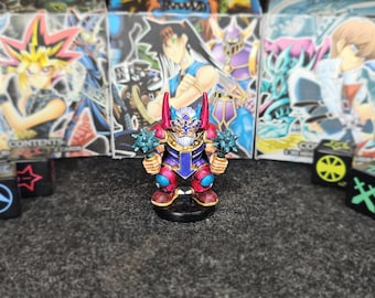 Op de afbeelding: Een miniatuurfiguur van een krijger, die twee knotsen vasthoudt. De figuur is beschilderd met rode, blauwe en gouden accenten. De achtergrond bevat dozen met anime-stijl illustraties en dobbelstenen.