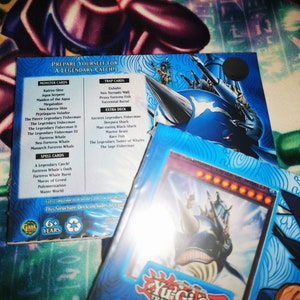 May include: A blue and white Yu-Gi-Oh! trading card game structure deck featuring a large blue whale with a ship on its back. The deck includes 60 cards and is recommended for ages 6 and up. The text on the box reads "Prepare yourself for a legendary catch!"