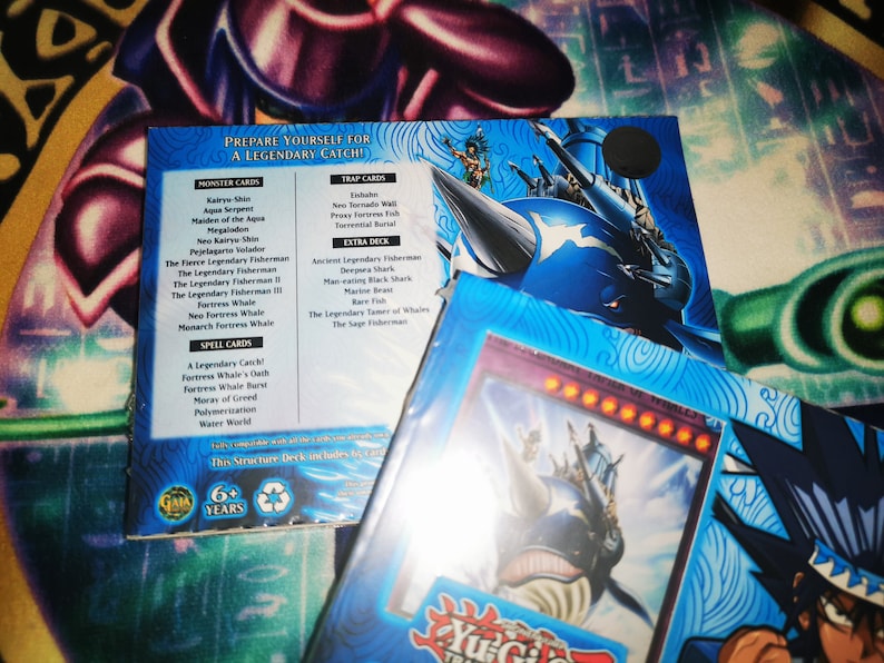 May include: A blue and white Yu-Gi-Oh! trading card game structure deck featuring a large blue whale with a ship on its back. The deck includes 60 cards and is recommended for ages 6 and up. The text on the box reads "Prepare yourself for a legendary catch!"