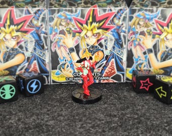 Könnte beinhalten: Eine rot-weiße Miniaturfigur steht auf einem schwarzen Sockel vor drei Schachteln mit Anime-Charakterkunst. Würfel mit Symbolen befinden sich auf beiden Seiten der Figur. Auf den Schachteln steht "1 3D MINIA" und "2 KARTEN".