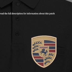 May include: Embroidered patch featuring the Porsche crest, a shield-shaped emblem with gold, red, blue, and black details. The text "STUTTGART" is visible within the crest. The patch is displayed on a black polo shirt. The text "Please read the full description for information about this patch" is above the patch.