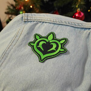 Puede incluir: Parche bordado de coraz&oacute;n verde con contorno negro y espinas en una chaqueta vaquera azul claro.