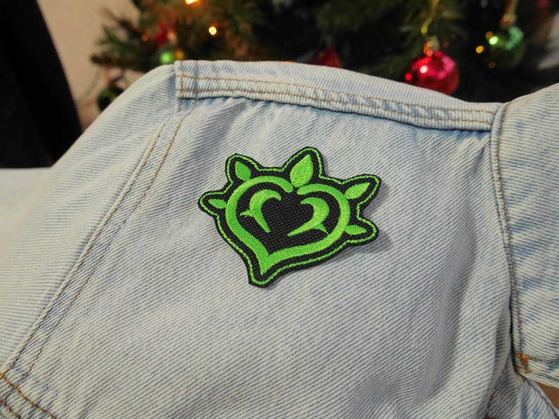 Puede incluir: Parche bordado de coraz&oacute;n verde con contorno negro y espinas en una chaqueta vaquera azul claro.