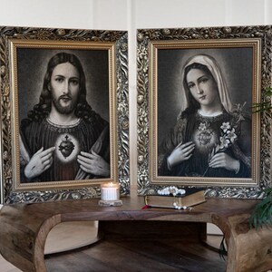 May include: Two framed black and white religious images with gold frames. The image on the left depicts Jesus with his heart exposed, and the image on the right depicts Mary with her heart exposed.