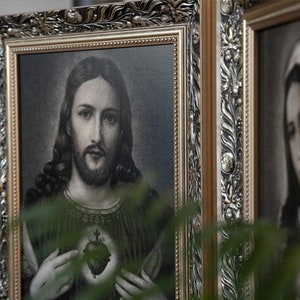 May include: A framed image of Jesus Christ with a heart and cross on his chest. The image is in black and white and has a gold frame.