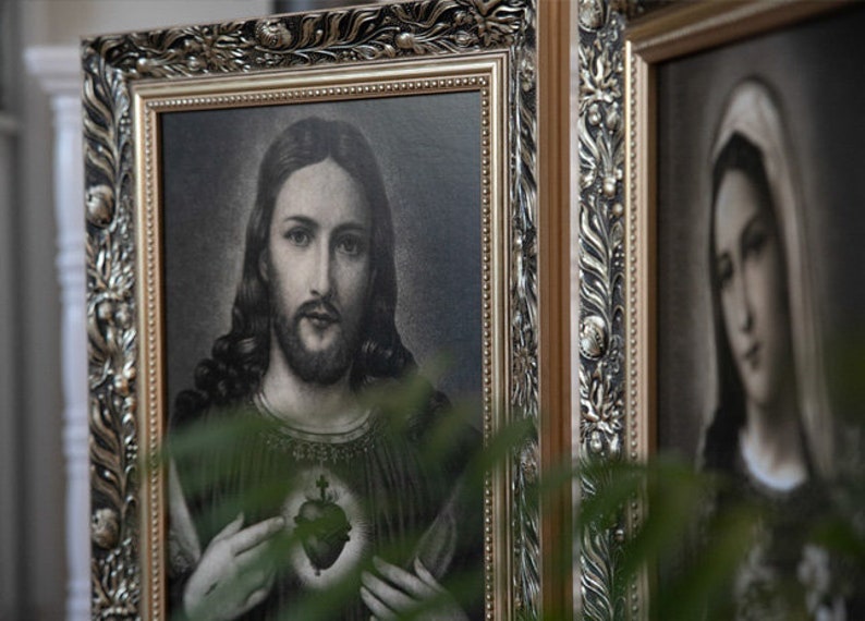 May include: A framed image of Jesus Christ with a heart and cross on his chest. The image is in black and white and has a gold frame.