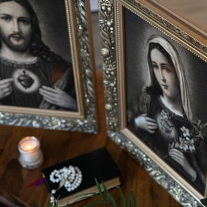 May include: Two framed religious paintings with ornate gold frames. The left painting depicts Jesus with a bleeding heart, and the right painting depicts Mary with a bleeding heart.