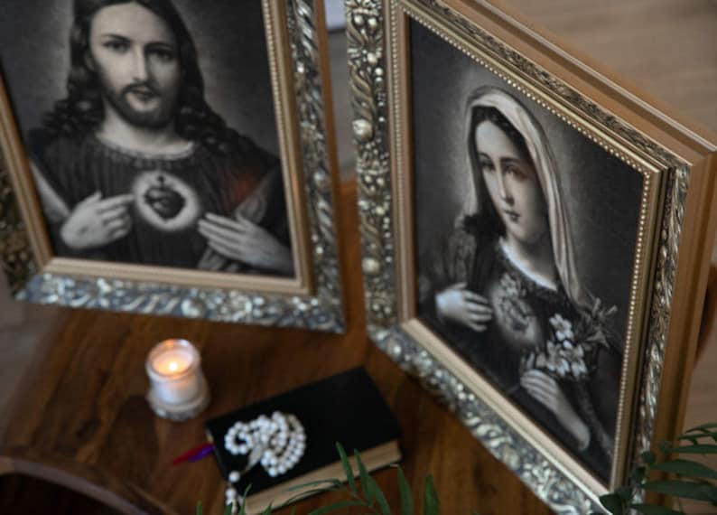 May include: Two framed religious paintings with ornate gold frames. The left painting depicts Jesus with a bleeding heart, and the right painting depicts Mary with a bleeding heart.