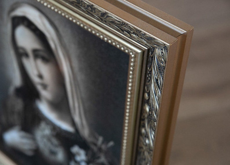 May include: A framed black and white portrait of a woman wearing a veil. The frame is ornate with gold accents and a beaded border.