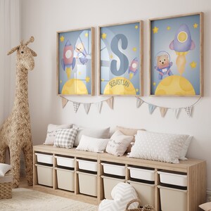 May include: Three framed prints with a blue background and yellow moon. Each print features a cartoon bear wearing a space suit and a rocket ship. The middle print has the name "Sebastian" written on it.