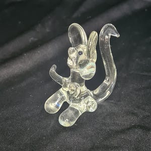 May include: A clear glass figurine of a monkey with a long tail. The monkey is sitting on its hind legs with its arms outstretched.