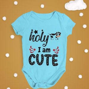 May include: A light blue baby grow with a black and white cow illustration and the text "holy I am CUTE" in black.