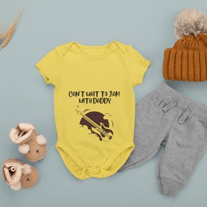 May include: Yellow baby onesie with short sleeves featuring a black and brown electric guitar graphic and the text "Can't wait to jam with Daddy".