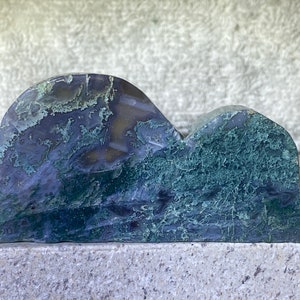 May include: A blue and green agate stone carved into the shape of two mountains. The stone has a natural, rough texture and is a beautiful example of the natural beauty of agate.