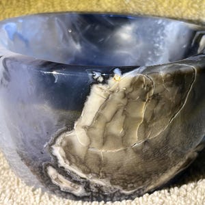 May include: A white, gray, and black agate bowl with a natural, organic shape. The bowl is made of polished stone and has a smooth, glossy finish.