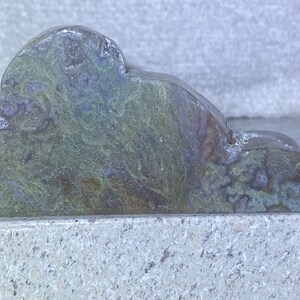 May include: A cloud-shaped decorative object carved from stone. The stone features a mix of green, blue, and brown hues, with a textured, organic pattern. The object is displayed on a light gray surface.