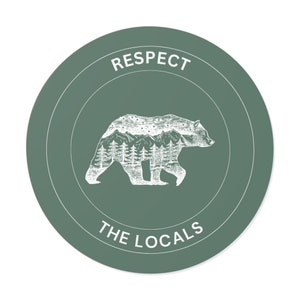 Puede incluir: Una pegatina circular verde con un contorno blanco. La pegatina presenta un oso blanco con una cordillera dentro de su cuerpo. El texto "RESPECT THE LOCALS" está escrito debajo del oso.