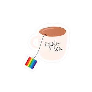 Può includere: Una tazza bianca con tè marrone all'interno e una bustina di tè arcobaleno appesa al bordo. La tazza dice "Equal-tea" in scrittura corsiva nera.